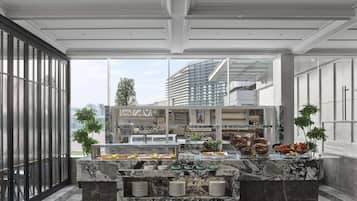 A modern kitchen with marble countertops, a buffet setup, and large windows offering views of the cityscape.