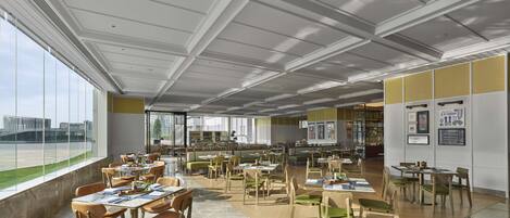 Un comedor espacioso y moderno con techos altos y grandes ventanales que ofrecen vistas al paisaje urbano.