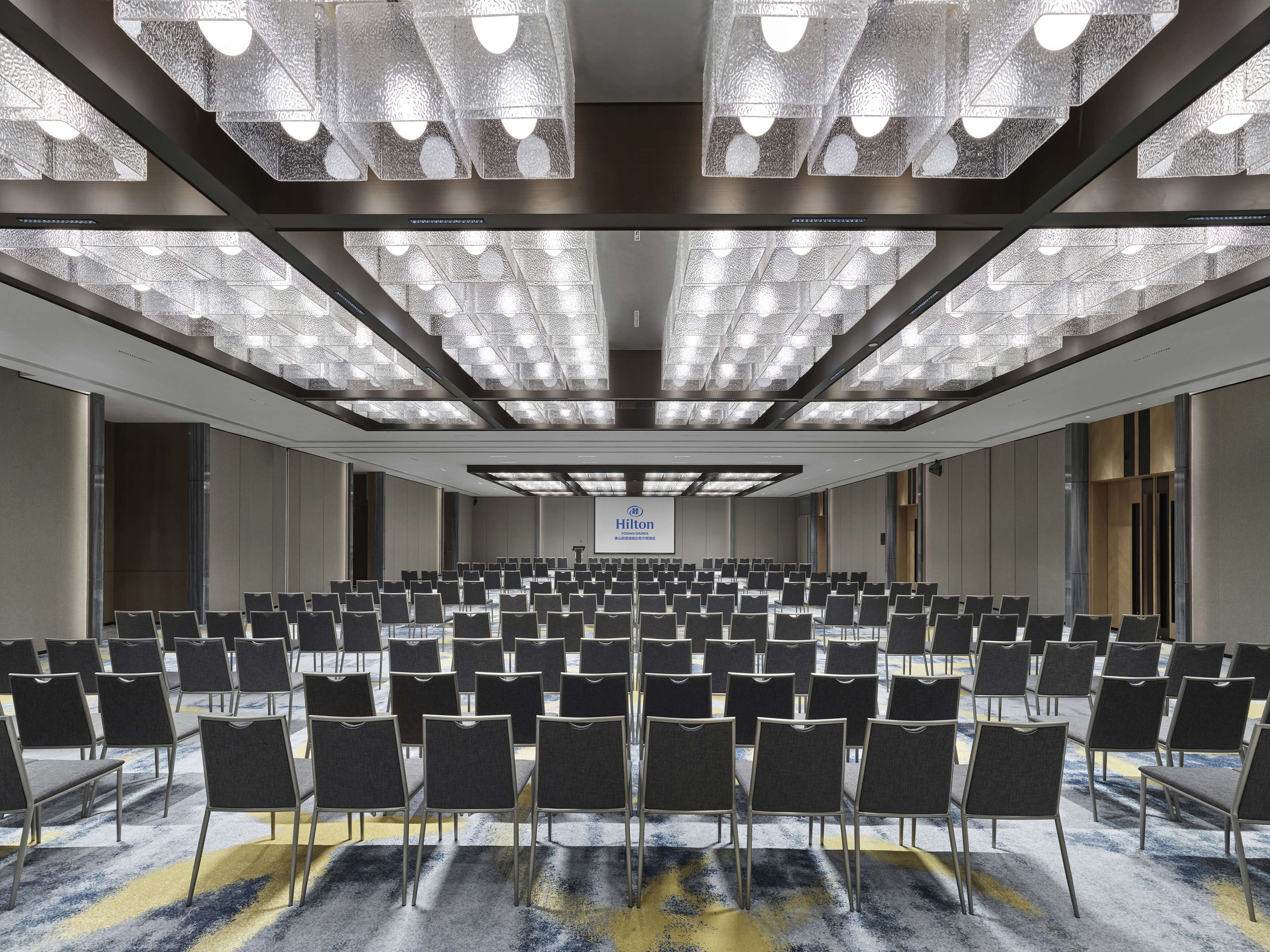 A conference room with rows of chairs, a large screen, and a ceiling with patterned lights.