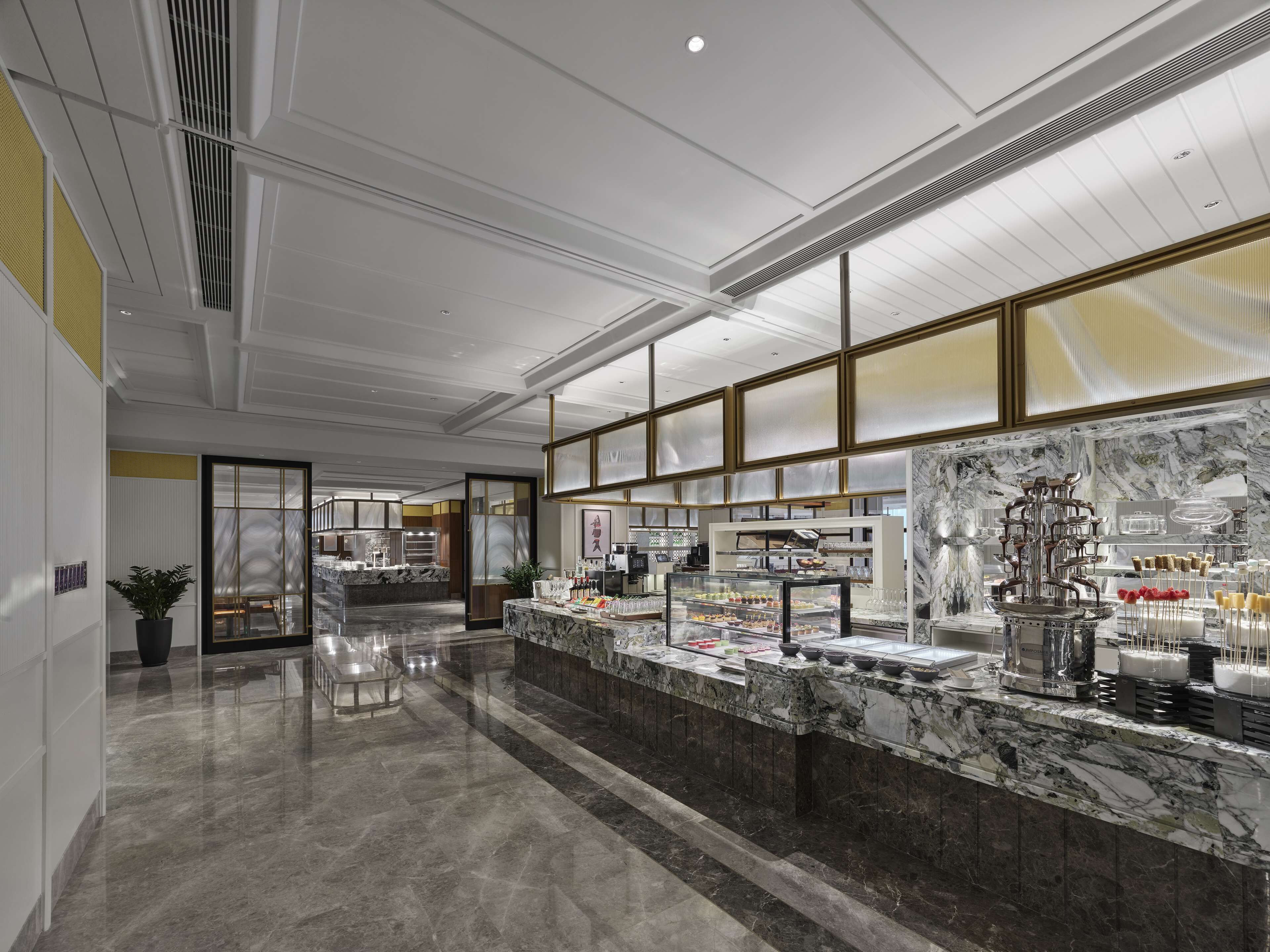 Un hall d’hôtel moderne avec un comptoir de réception en marbre, une grande vitrine et un espace salon agrémenté d’une plante.
