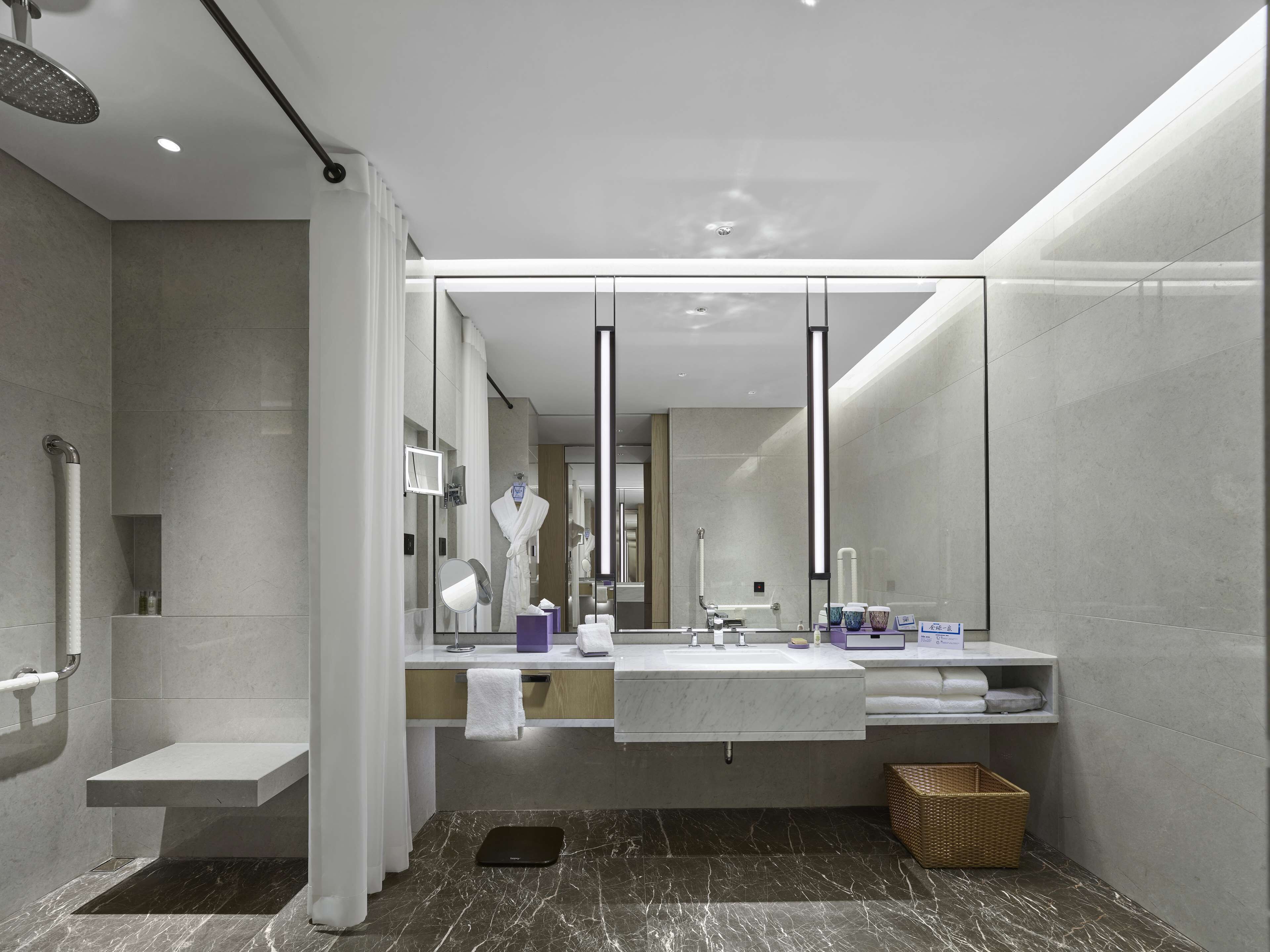 A modern bathroom with a large mirror, two sinks, a shower area, and a vanity with toiletries.