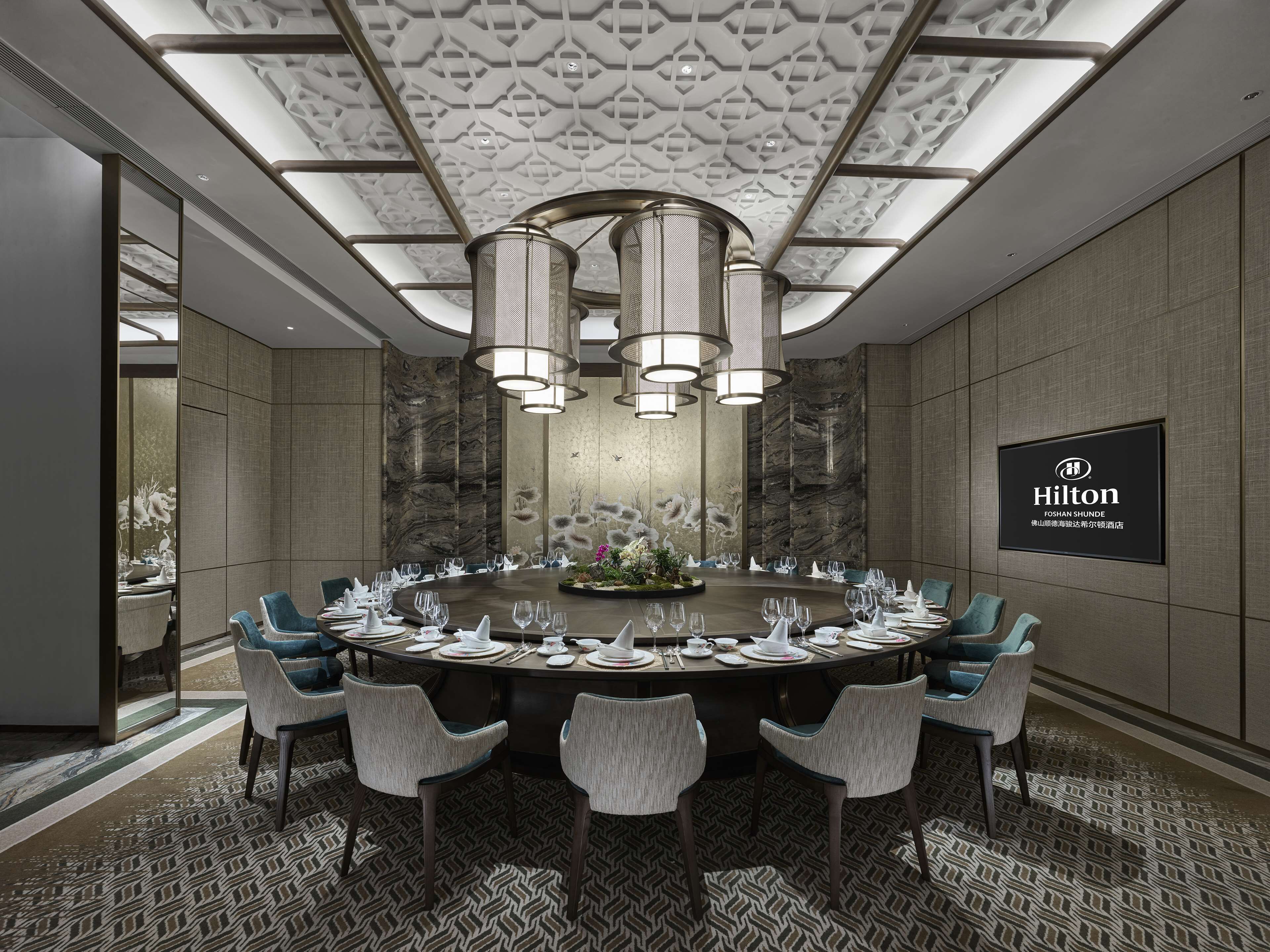 A conference room with a round table, chairs, and a large screen displaying the Hilton logo.