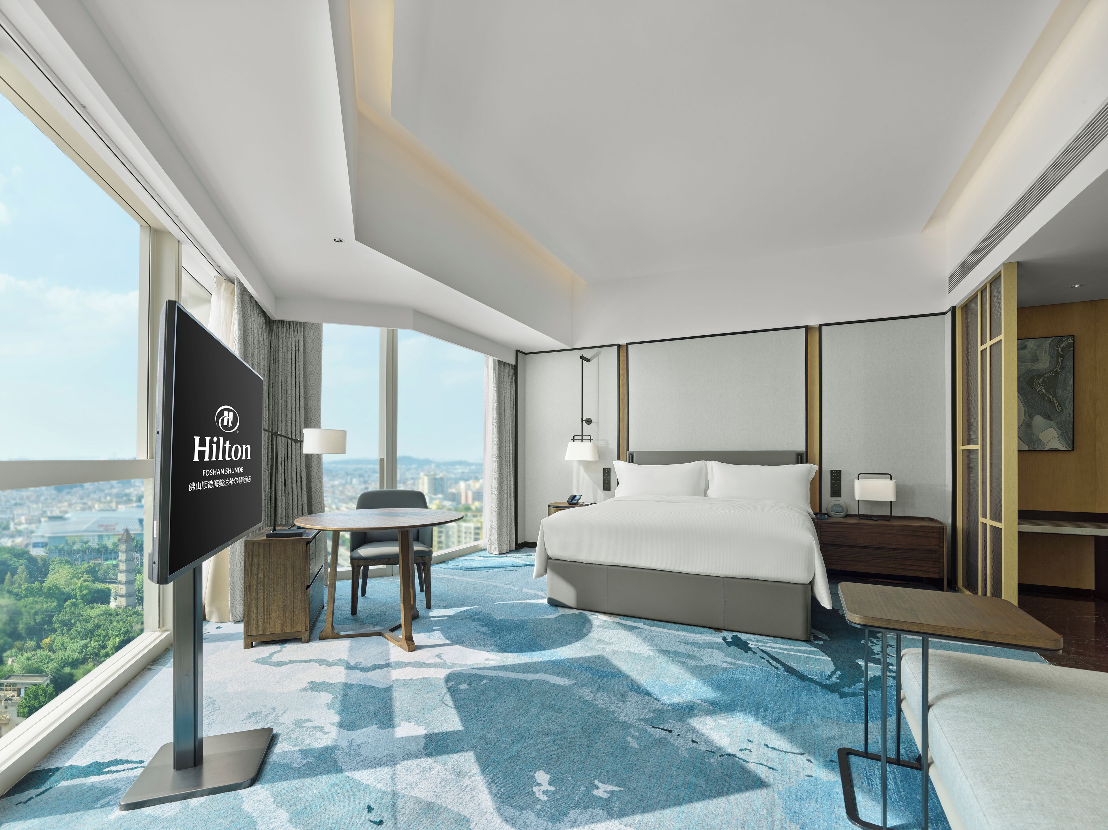 A hotel room with a bed, bedside table, lamp, and a desk with a chair.