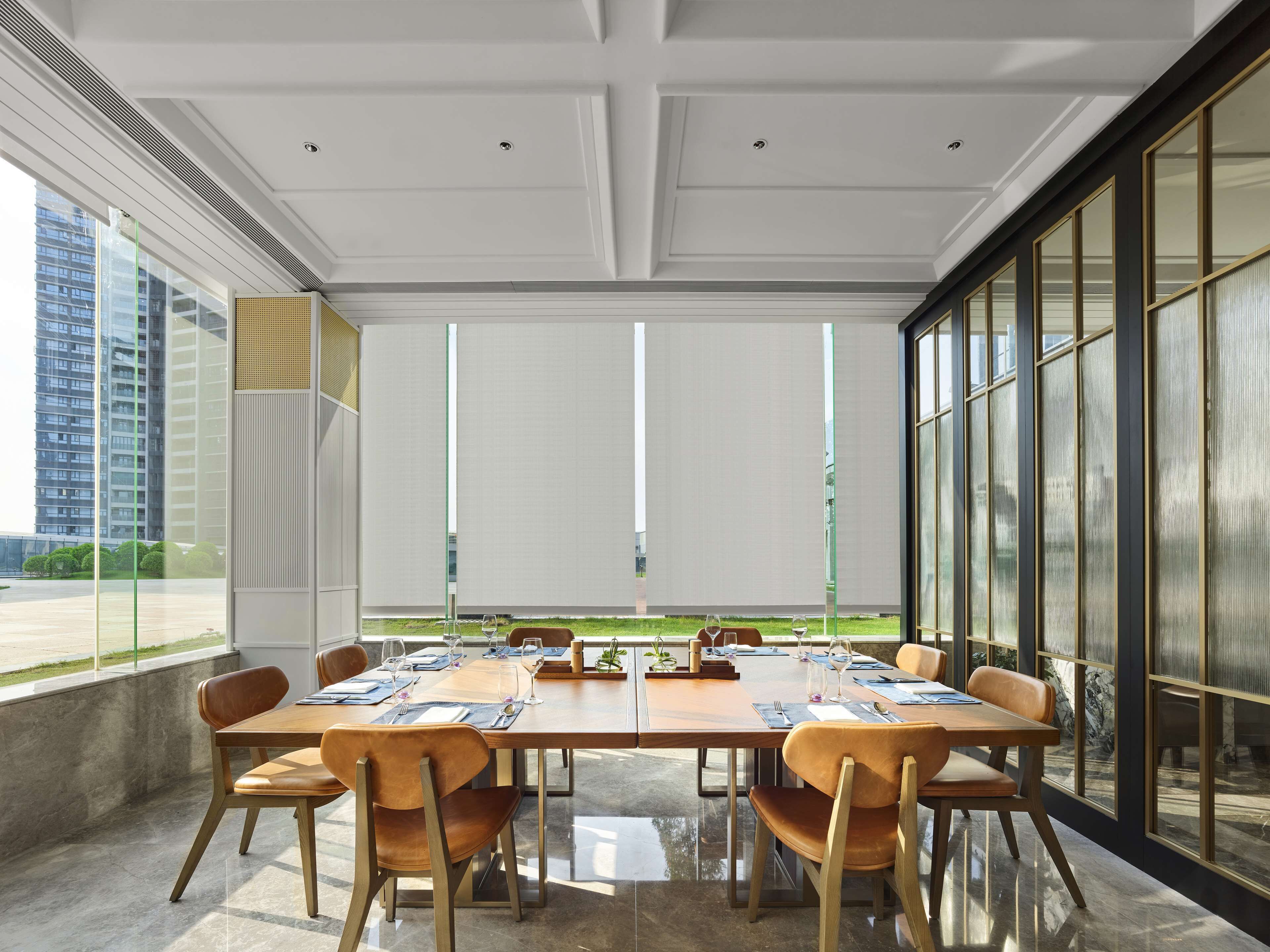 A conference room with a long table, chairs, and a view of a building through large windows.