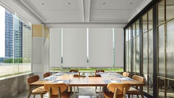 A conference room with a long table, chairs, and a view of a building through large windows.