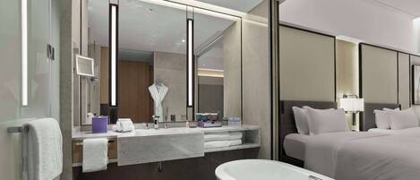 A modern hotel room with a large mirror, a bathtub, a bed with white linens, and a vanity with a mirror and a sink.