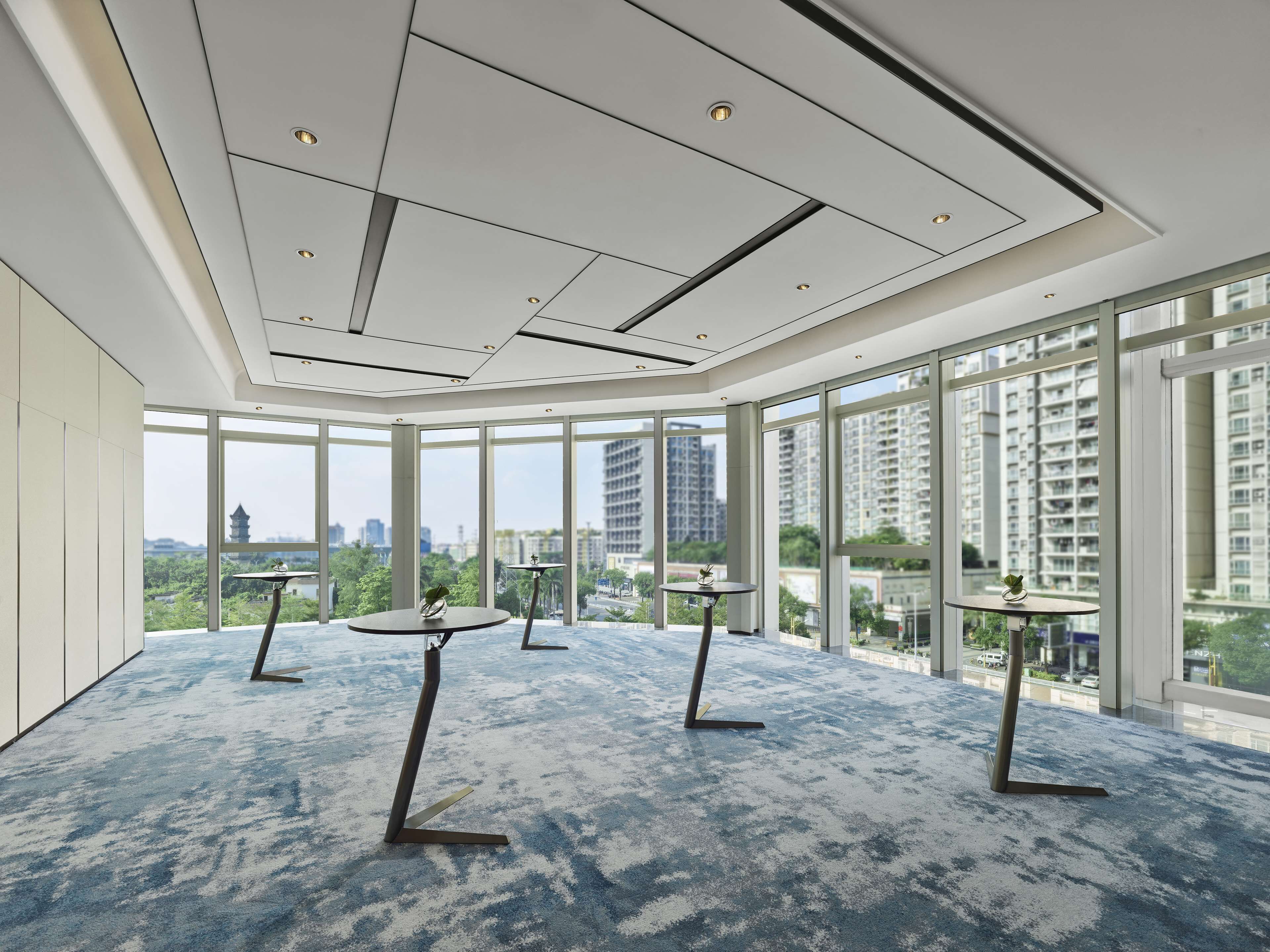 A spacious room with large windows, a modern ceiling design, and a blue carpet.