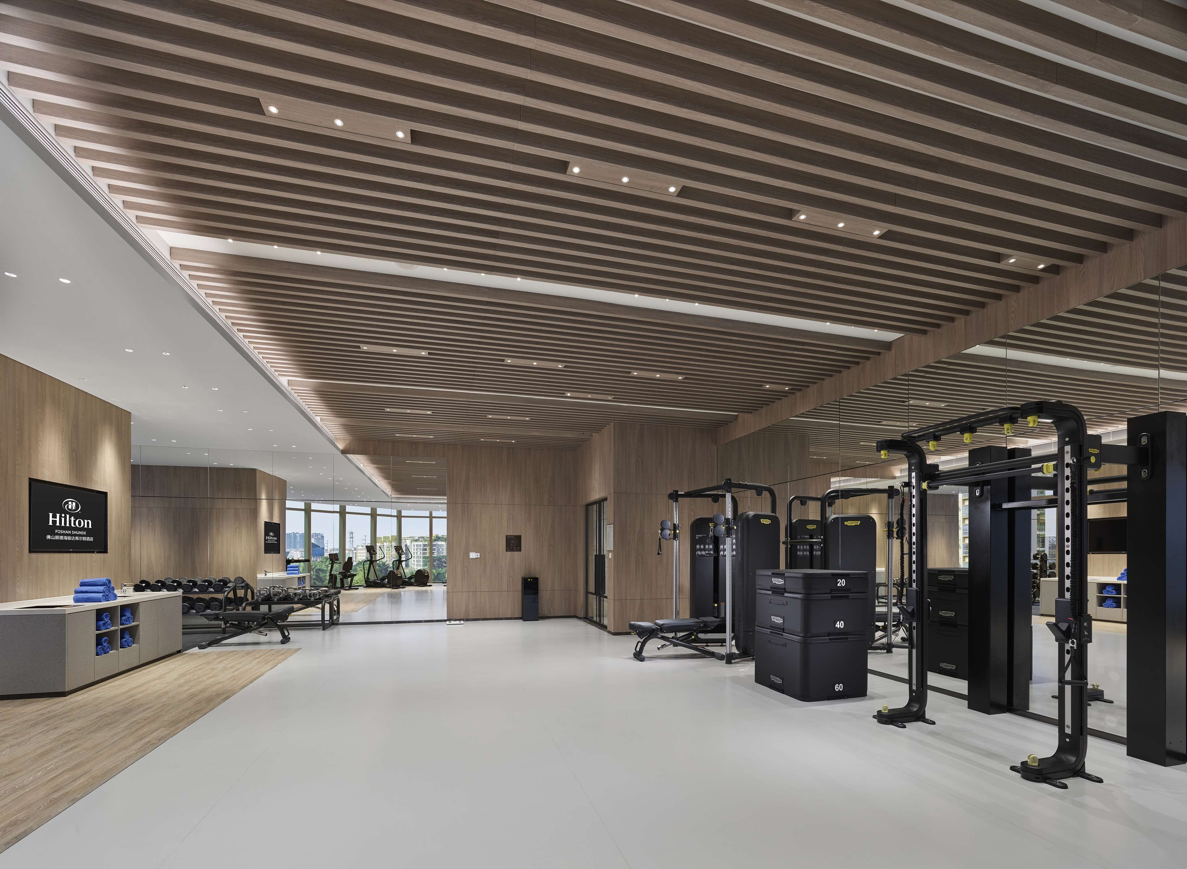 A modern hotel gym with wooden paneling, exercise equipment, and a view of the city through large windows.