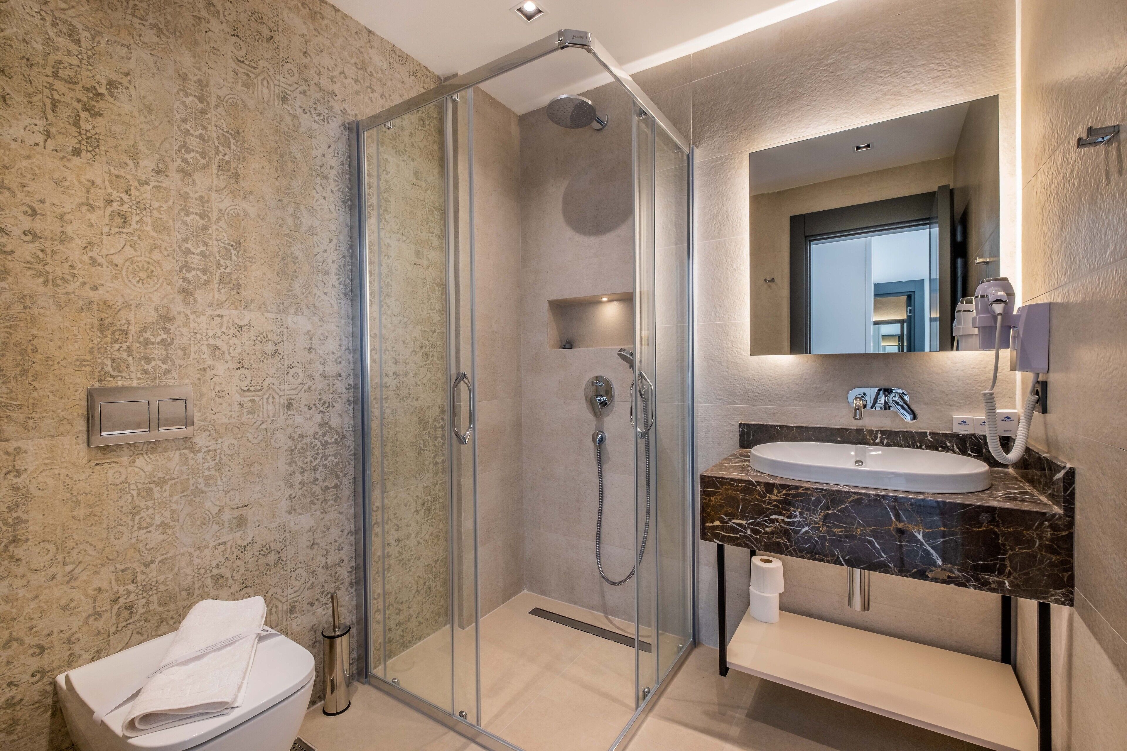 A modern bathroom with a glass-enclosed shower, a marble sink, and a large mirror.