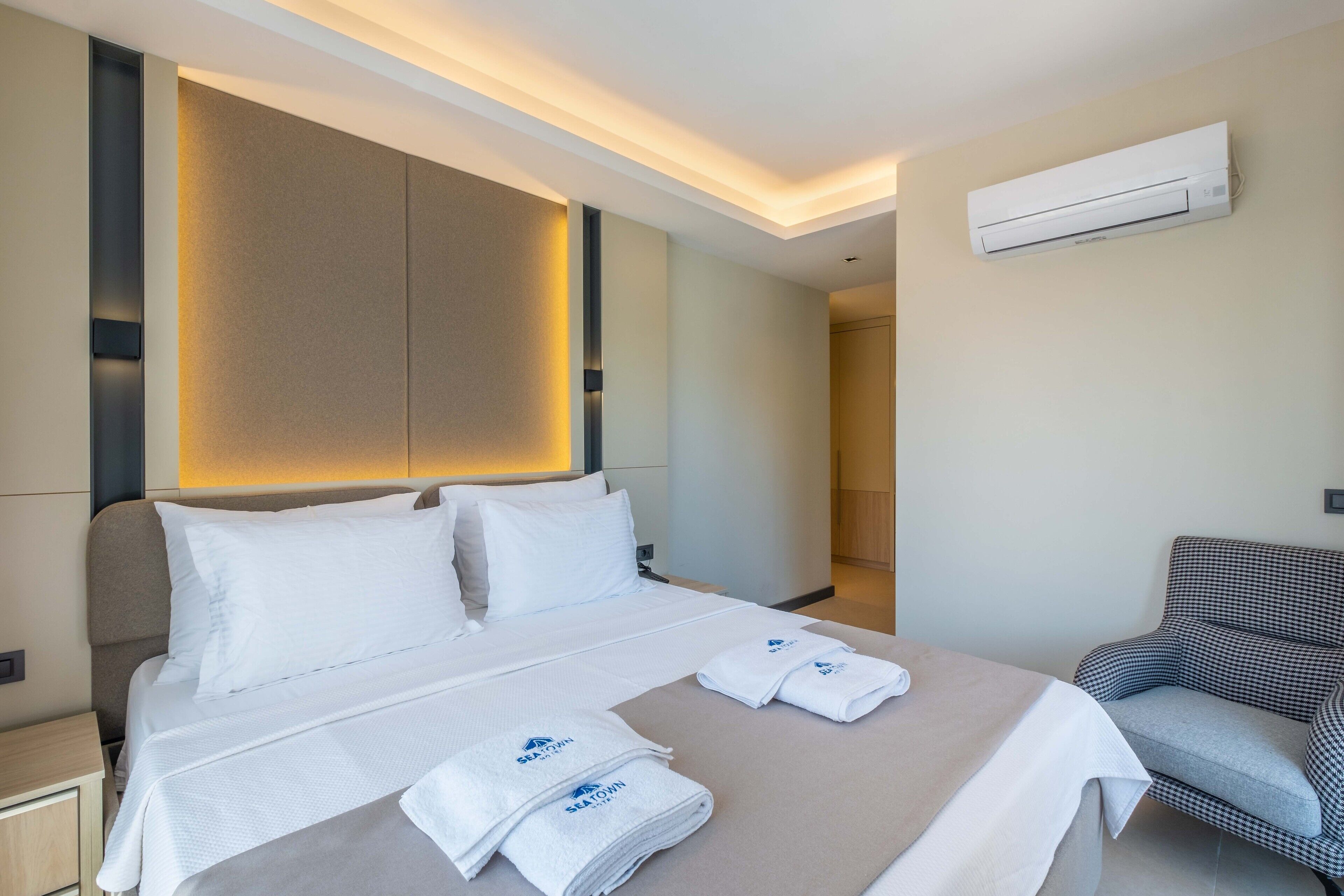 Una habitación de hotel moderna con una cama bien hecha, un sillón a cuadros y un aire acondicionado de pared.