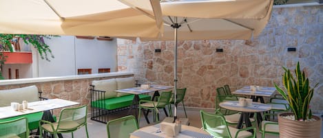 Une terrasse extérieure avec des tables et des chaises, des murs en pierre et des plantes en pot.