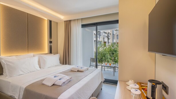 A hotel room with a bed, a desk with a coffee maker, and a view of the city through a balcony. - Seatown Hotel (Kas)
