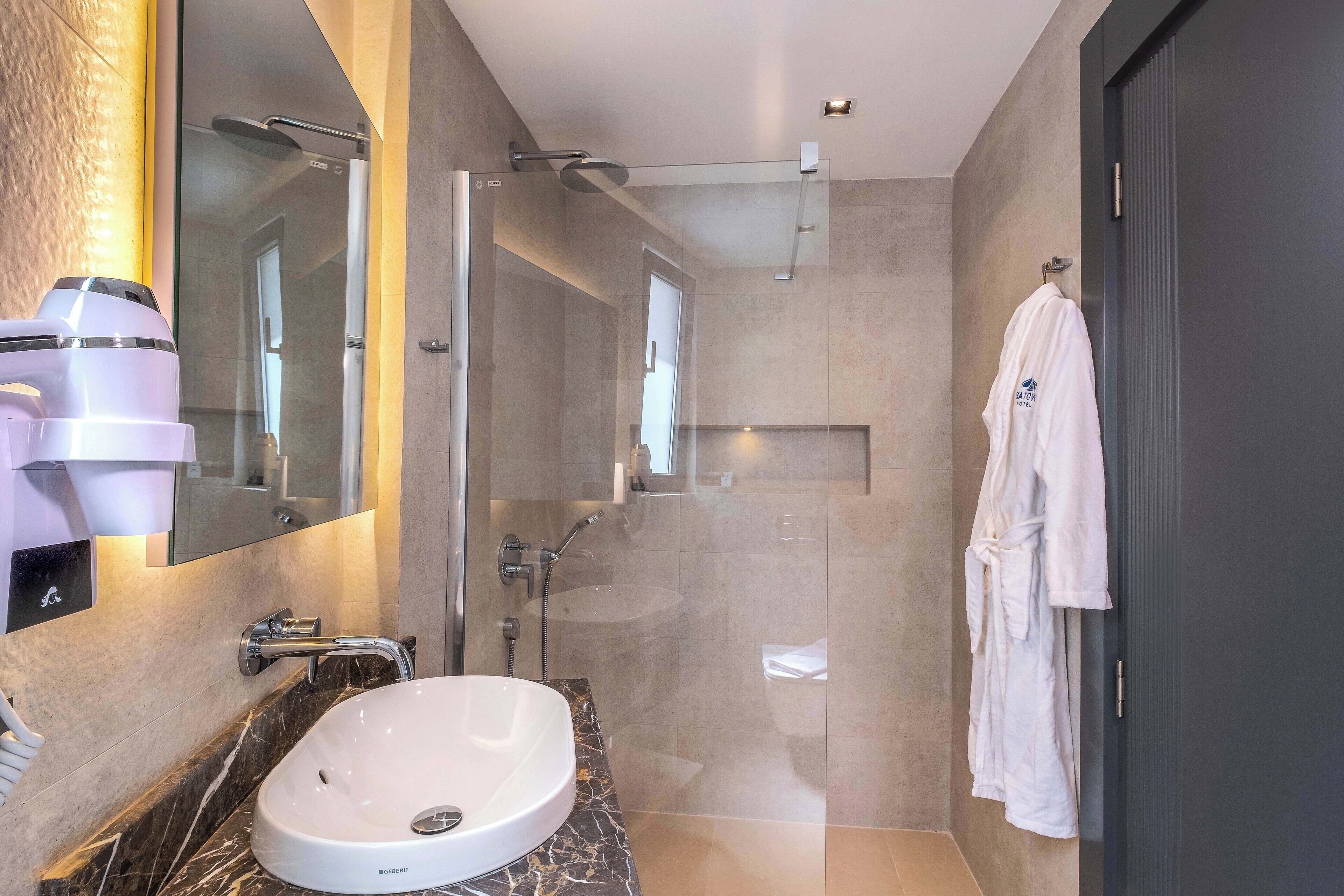 Un bagno moderno con un lavabo in marmo, una doccia con pareti in vetro e un accappatoio bianco appeso al muro.