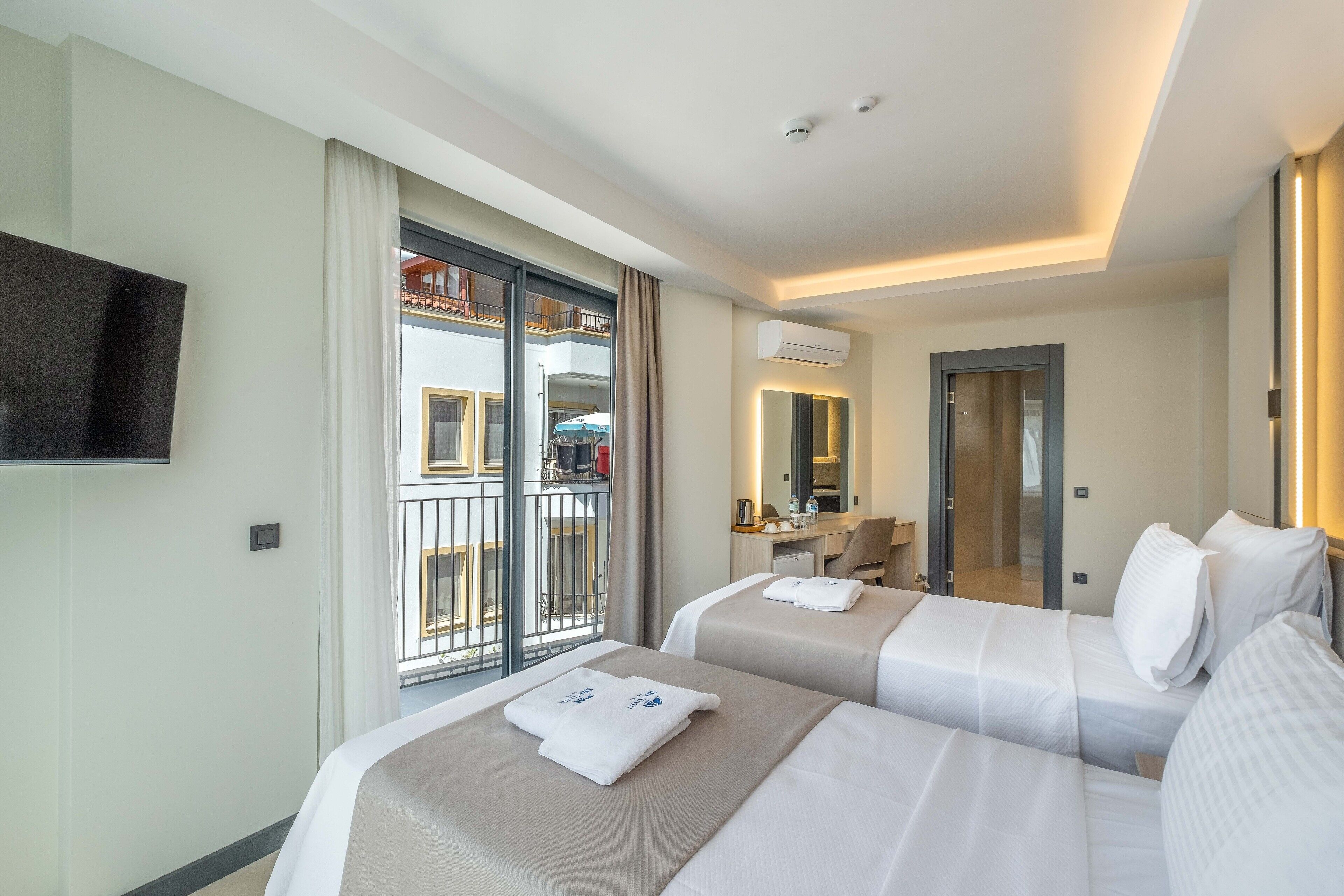 Habitación de hotel con dos camas, televisión, balcón con vistas y escritorio con silla.