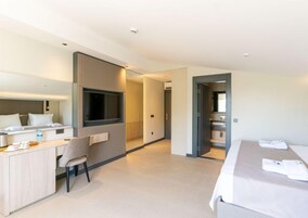 Una habitación de hotel moderna con una cama, un escritorio, una silla, un televisor y un baño visible a través de una puerta abierta.