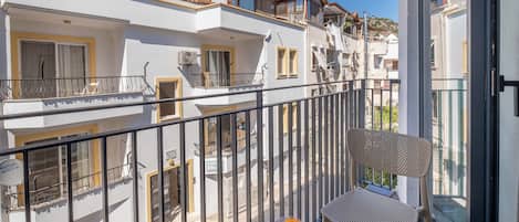 Un balcón con una mesa y dos vasos de jugo de naranja, con vistas a una zona residencial con varios edificios y montañas al fondo.