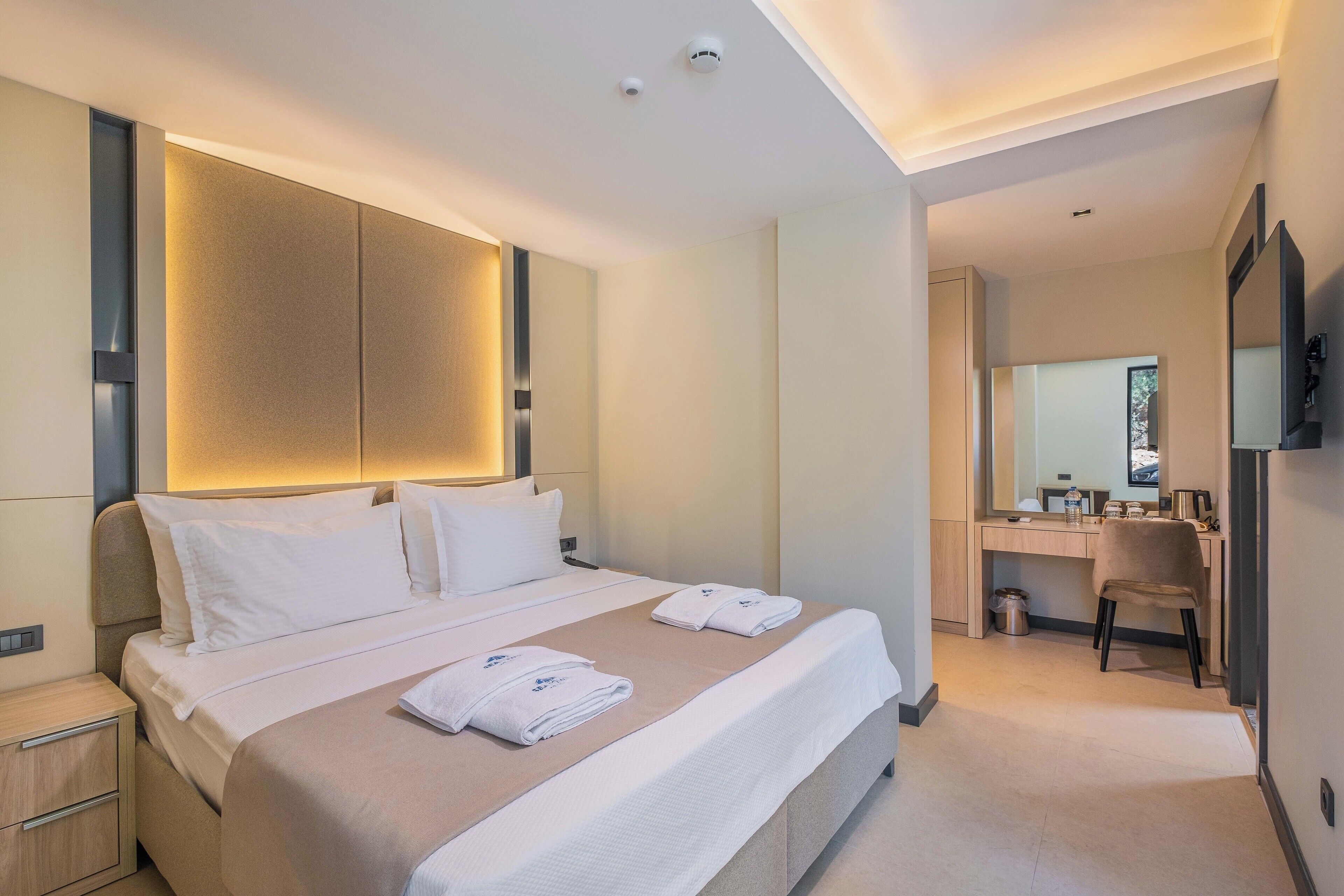 A modern hotel room with a large bed, a desk, and a mirror.