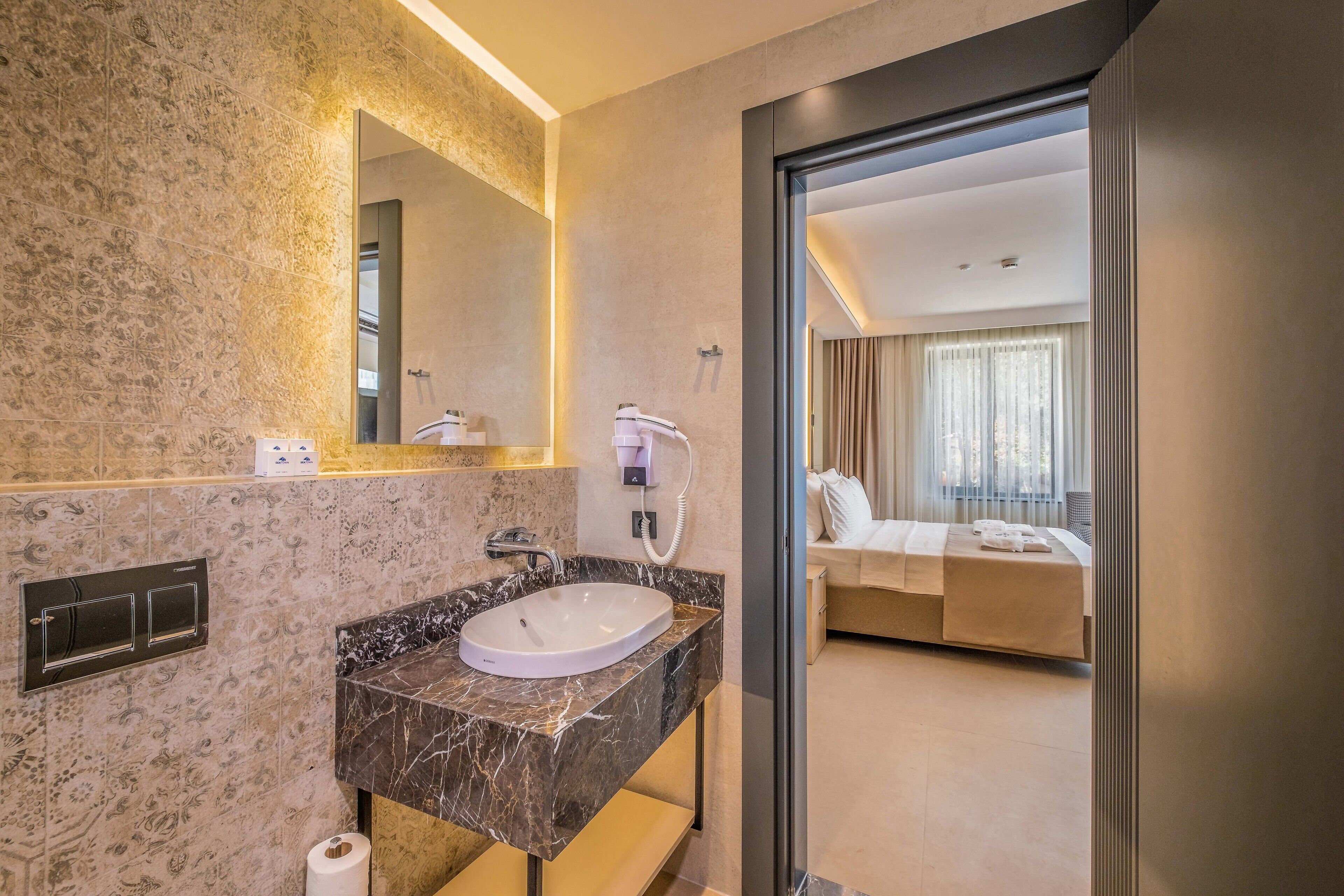 Un baño moderno con lavamanos de mármol, un espejo grande y una zona de ducha visible.