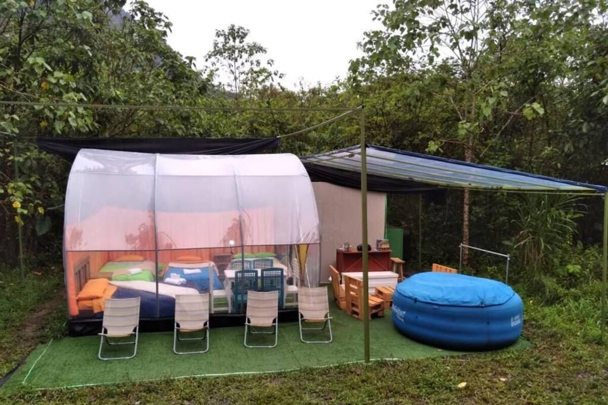 Een tentaccomodatie buiten met een bed, stoelen en een tafel.