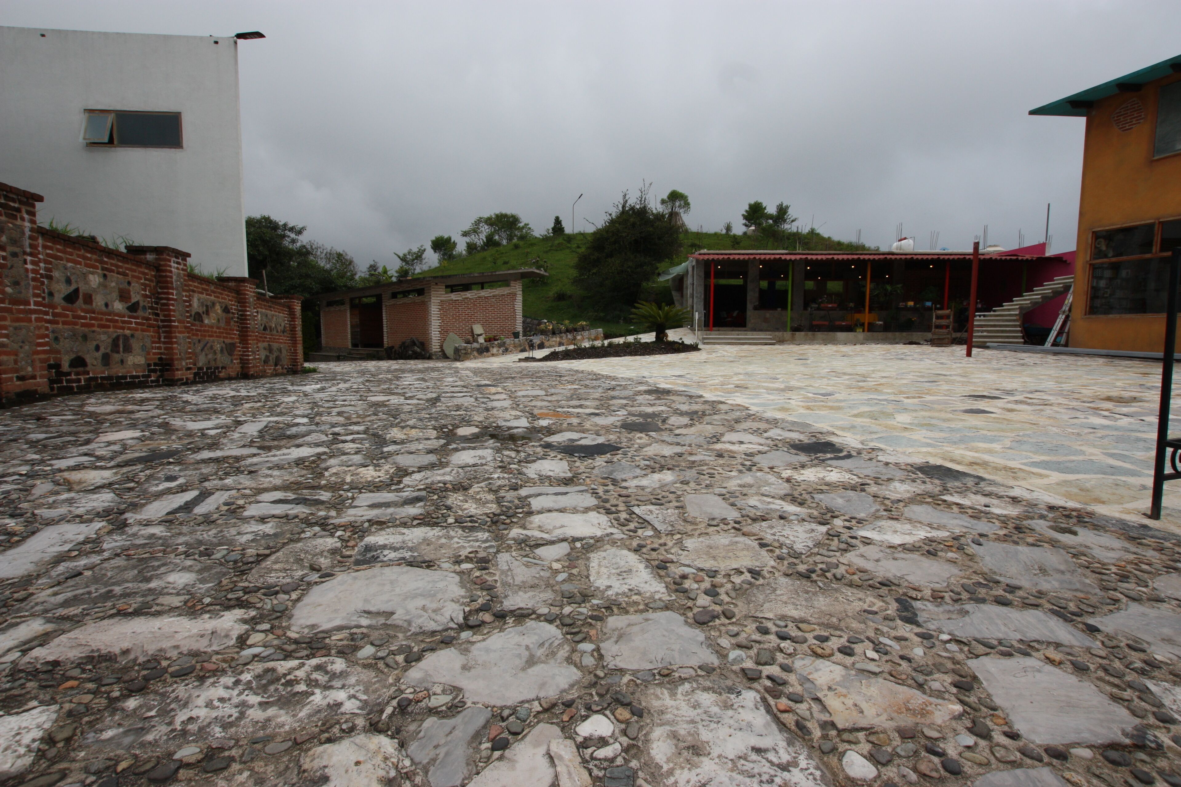 Un patio con suelo de piedra, pared de ladrillo y un edificio con tejado rojo.