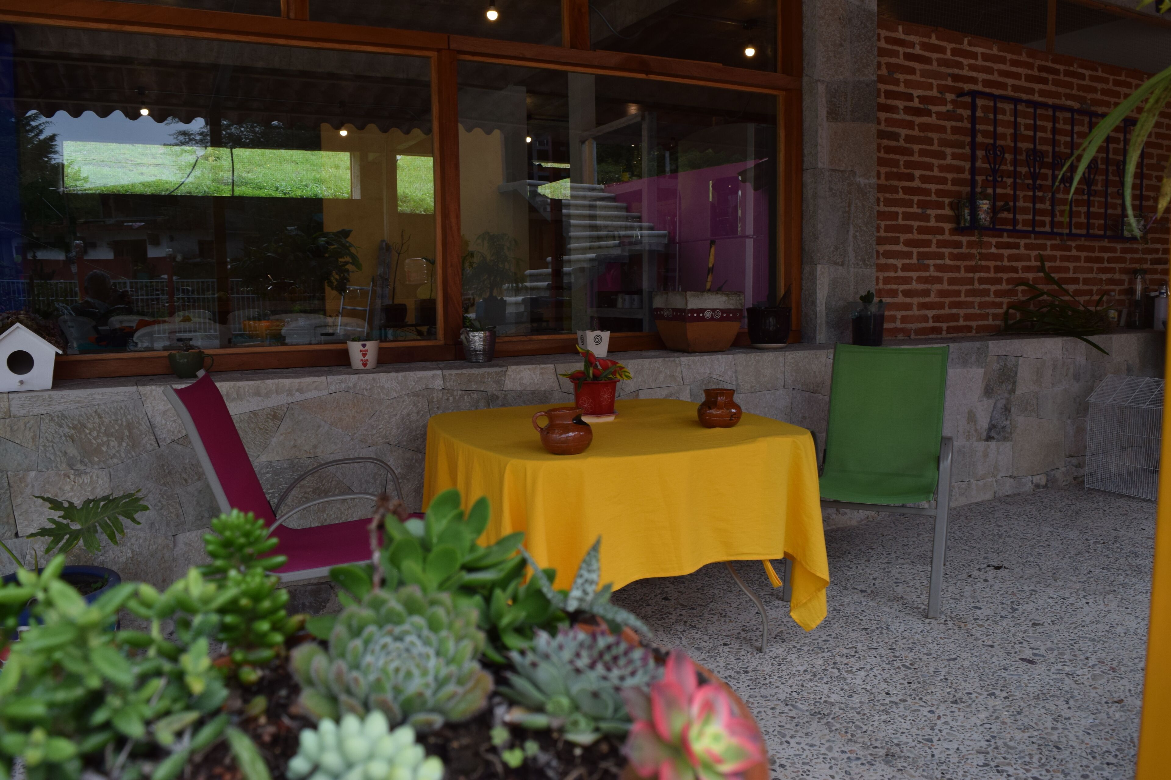 An outdoor patio area with a yellow table, potted plants, and a brick wall.