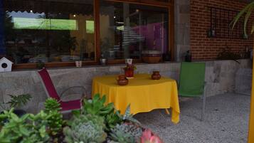 Un patio al aire libre con una mesa amarilla, plantas en macetas y un muro de ladrillo.