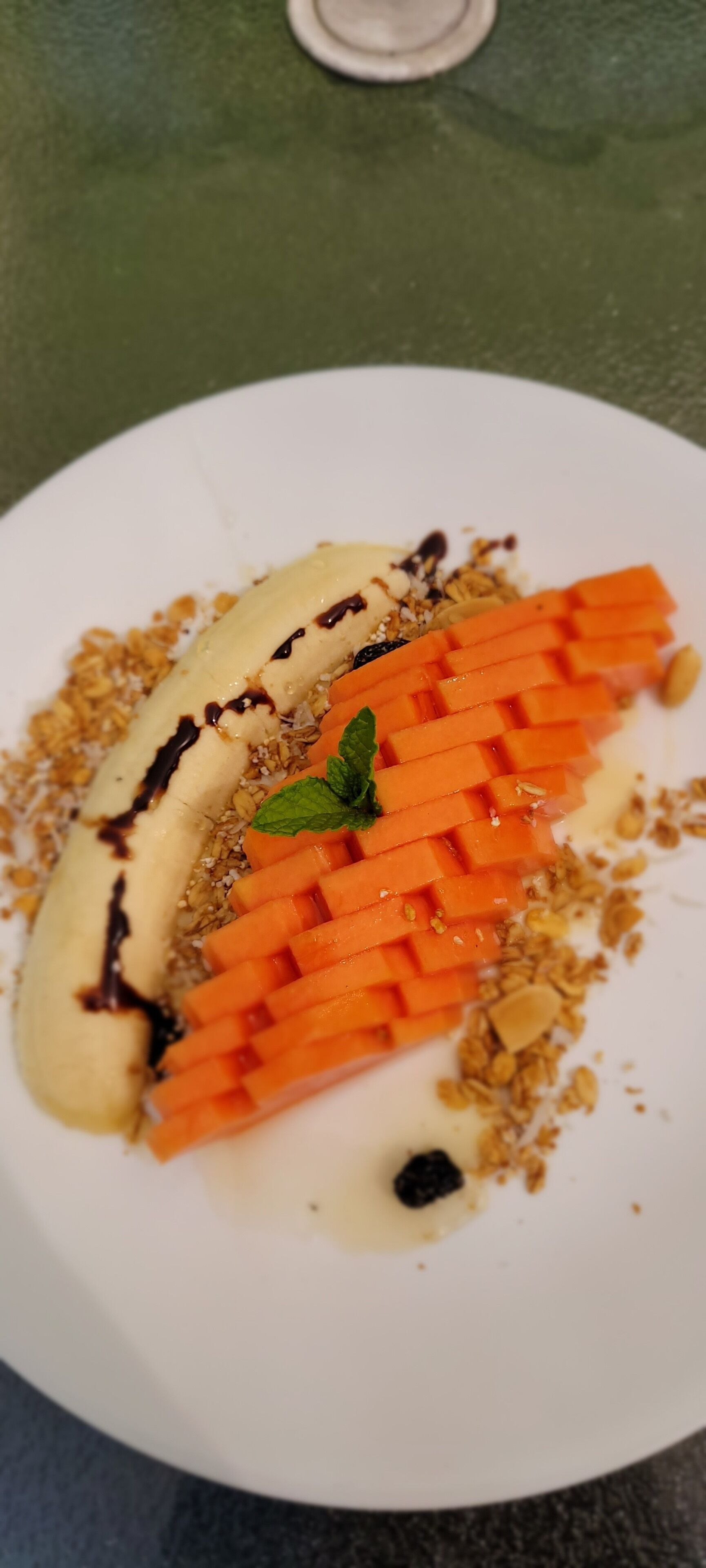 A dessert plate with a banana, carrot sticks, granola, and a mint leaf.
