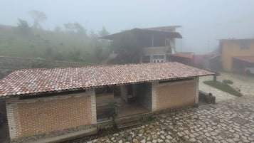 Un edificio de ladrillo con tejado de tejas, una escalera que sube al segundo piso y un coche estacionado cerca.