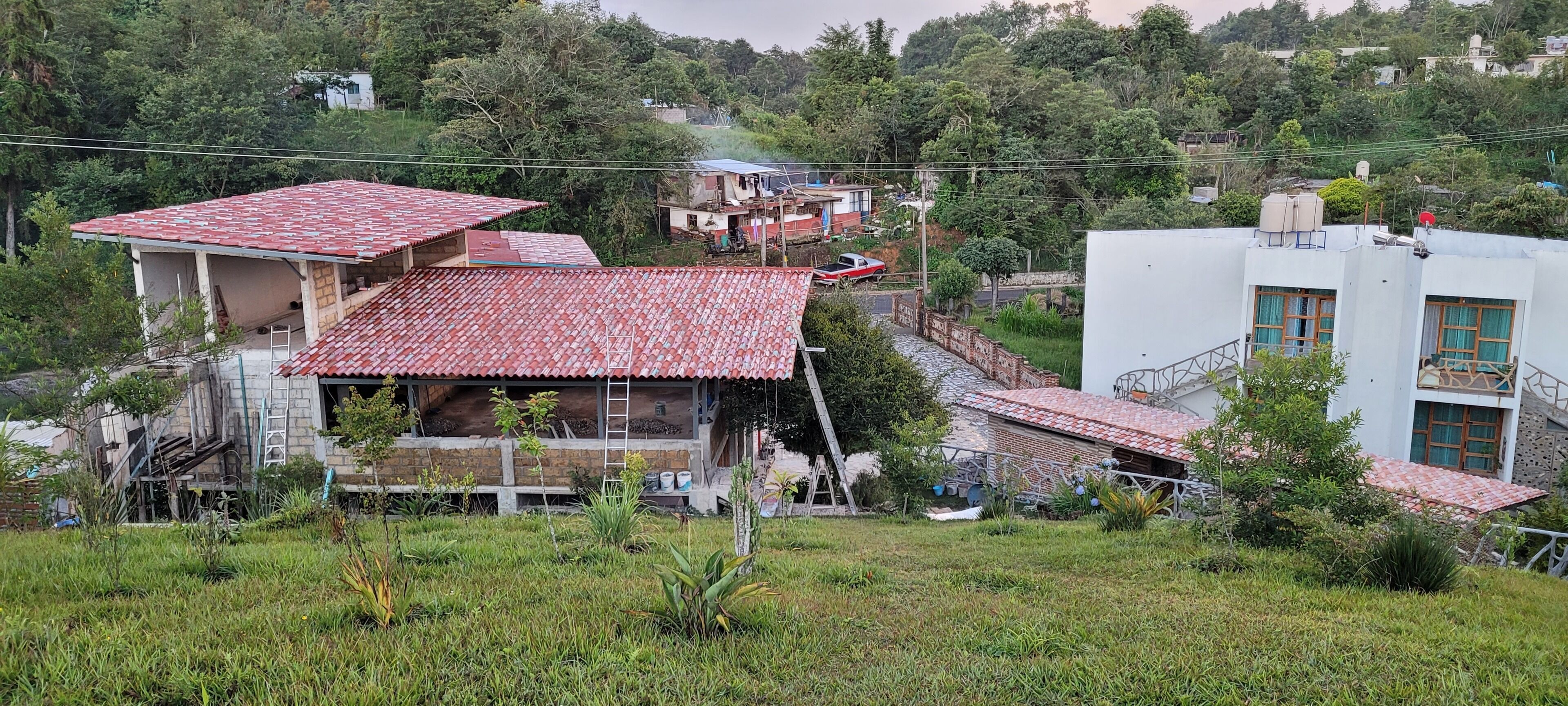 A residential area with houses, some under construction, and a white building with a red roof.