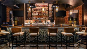 A bar area with a brick wall, shelves of liquor bottles, and bar stools.