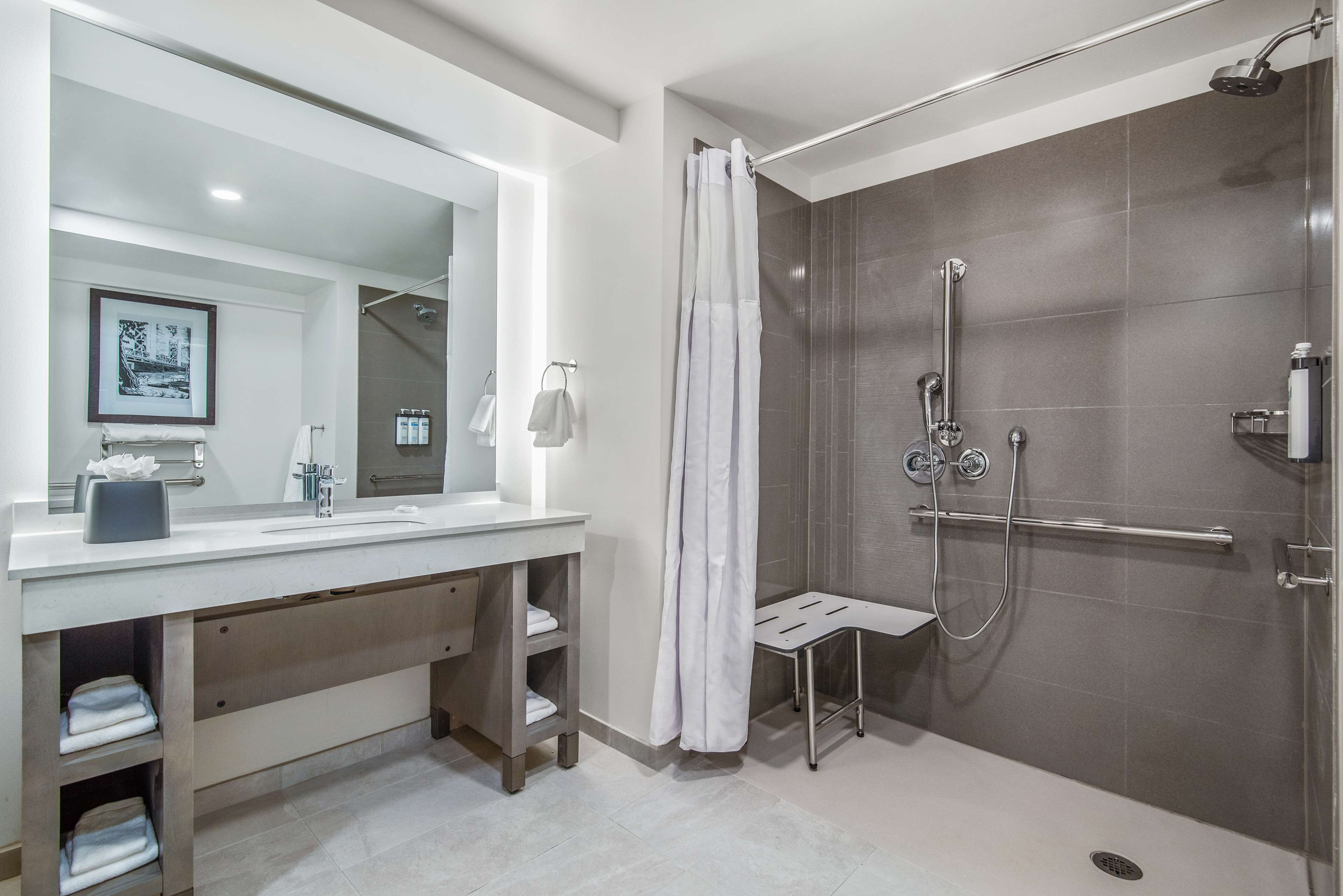 A modern bathroom with a large mirror, white vanity, and a walk-in shower with a glass door.