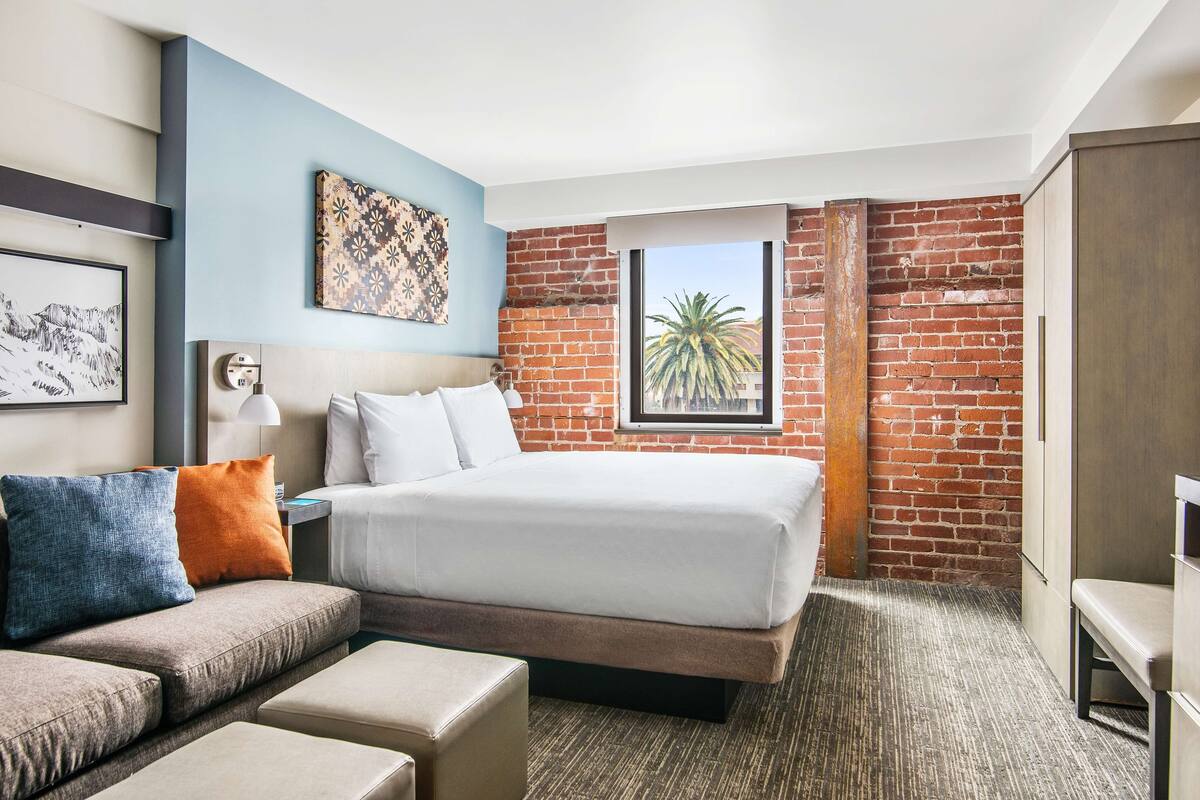Een hotelkamer met een bed, een bank, een tafeltje en een raam met uitzicht op palmbomen.