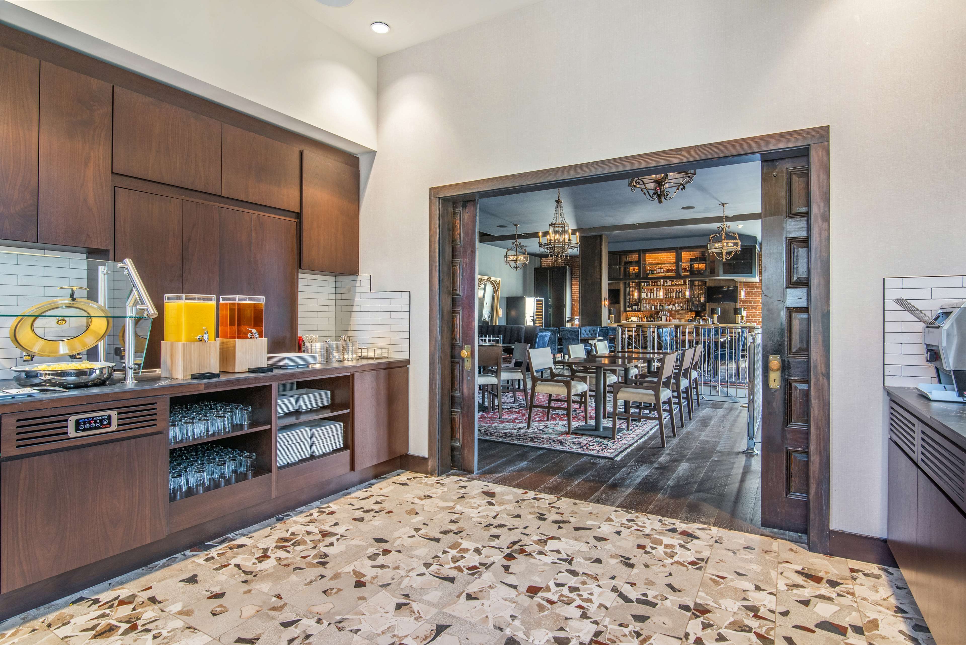 A modern kitchen with a built-in bar area, featuring a countertop with glasses and a wine cooler, and a dining area with a chandelier and bar stools.
