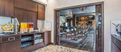 A modern kitchen with a built-in bar area, featuring a countertop with glasses and a wine cooler, and a dining area with a chandelier and bar stools.