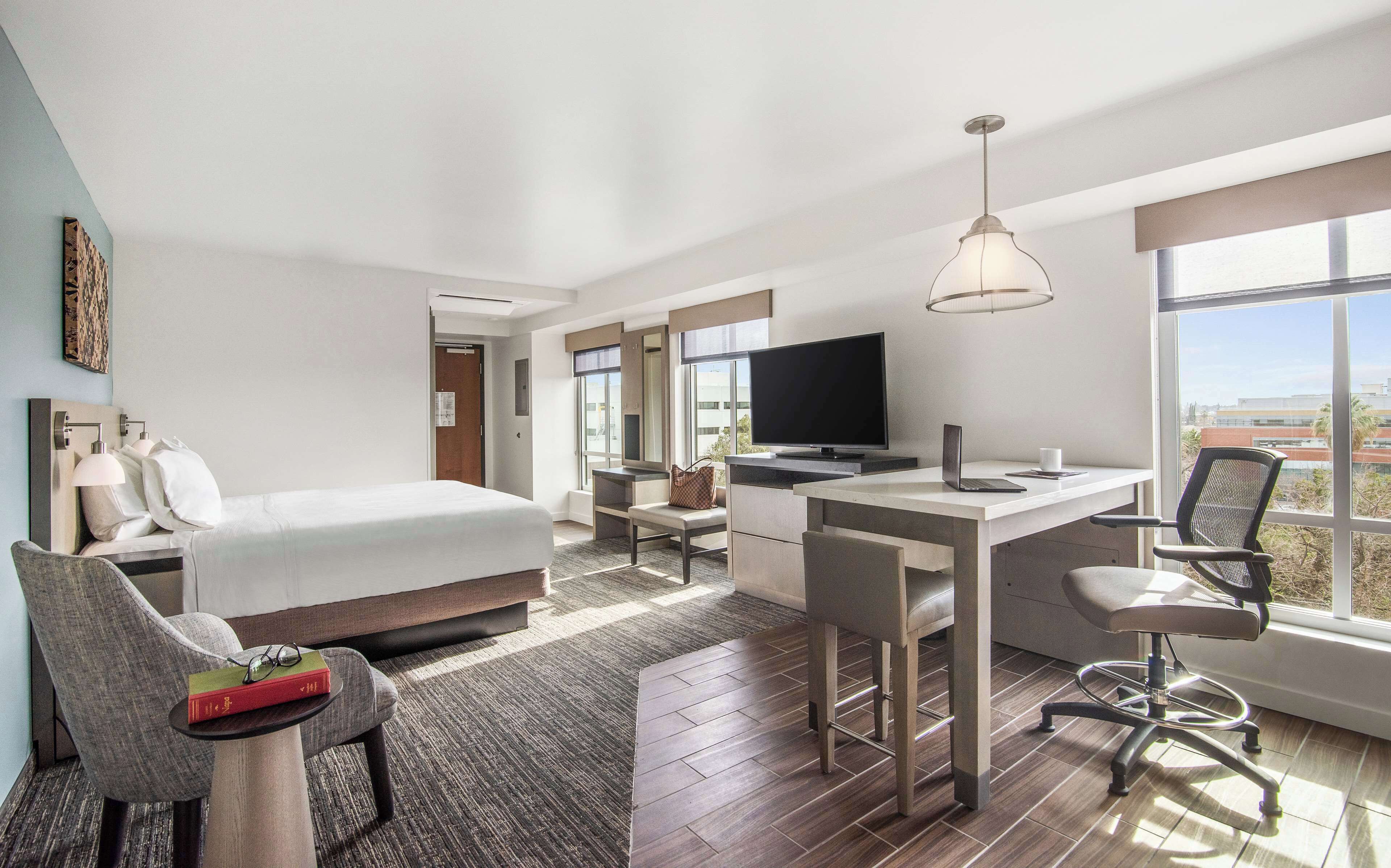 A modern hotel room with a bed, desk, and TV.