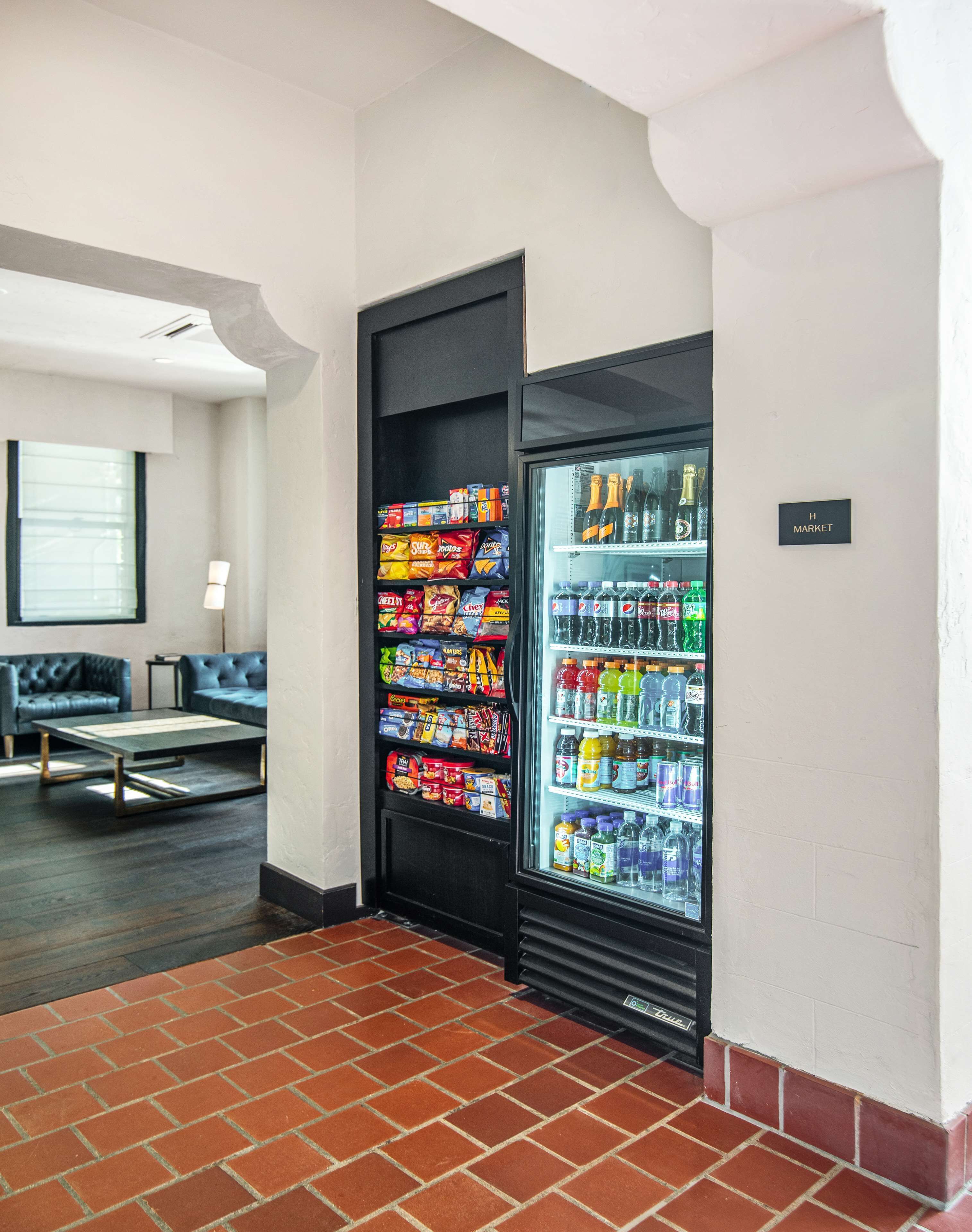 Máquina expendedora con aperitivos y bebidas, zona de estar con sofá y mesa, y un letrero que dice 'H MARKET'.