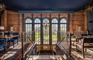 A spacious room with a brick wall, large arched windows, a chandelier, and a staircase leading to an outdoor area. - Hyatt House Sacramento/Midtown (Sacramento)