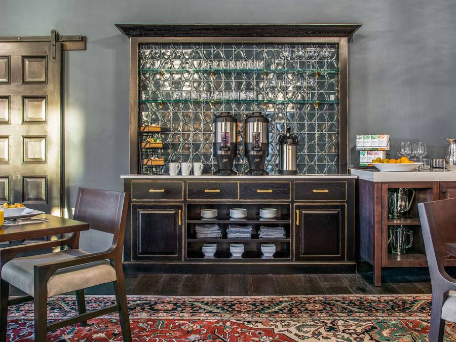 A modern kitchen with a built-in coffee station, a dining area with chairs and a table, and a patterned rug.