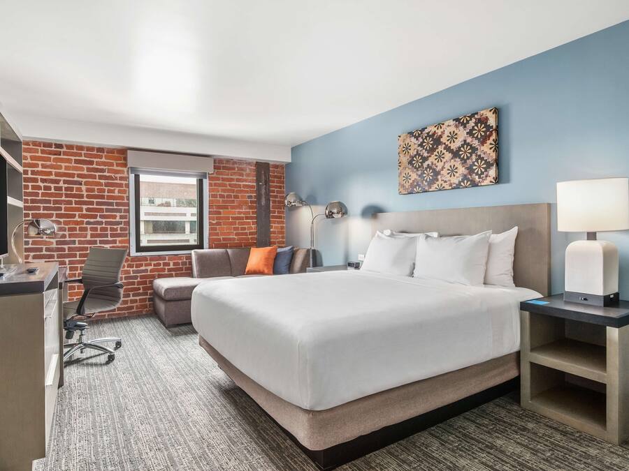 A hotel room with a large bed, a desk with a computer, a chair, and a window with a view.
