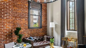 A living room with a brick wall, leather sofa, round coffee table, and a chandelier.