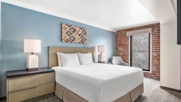 A hotel room with a large bed, two bedside tables with lamps, a headboard, a window with a view, and a brick accent wall.