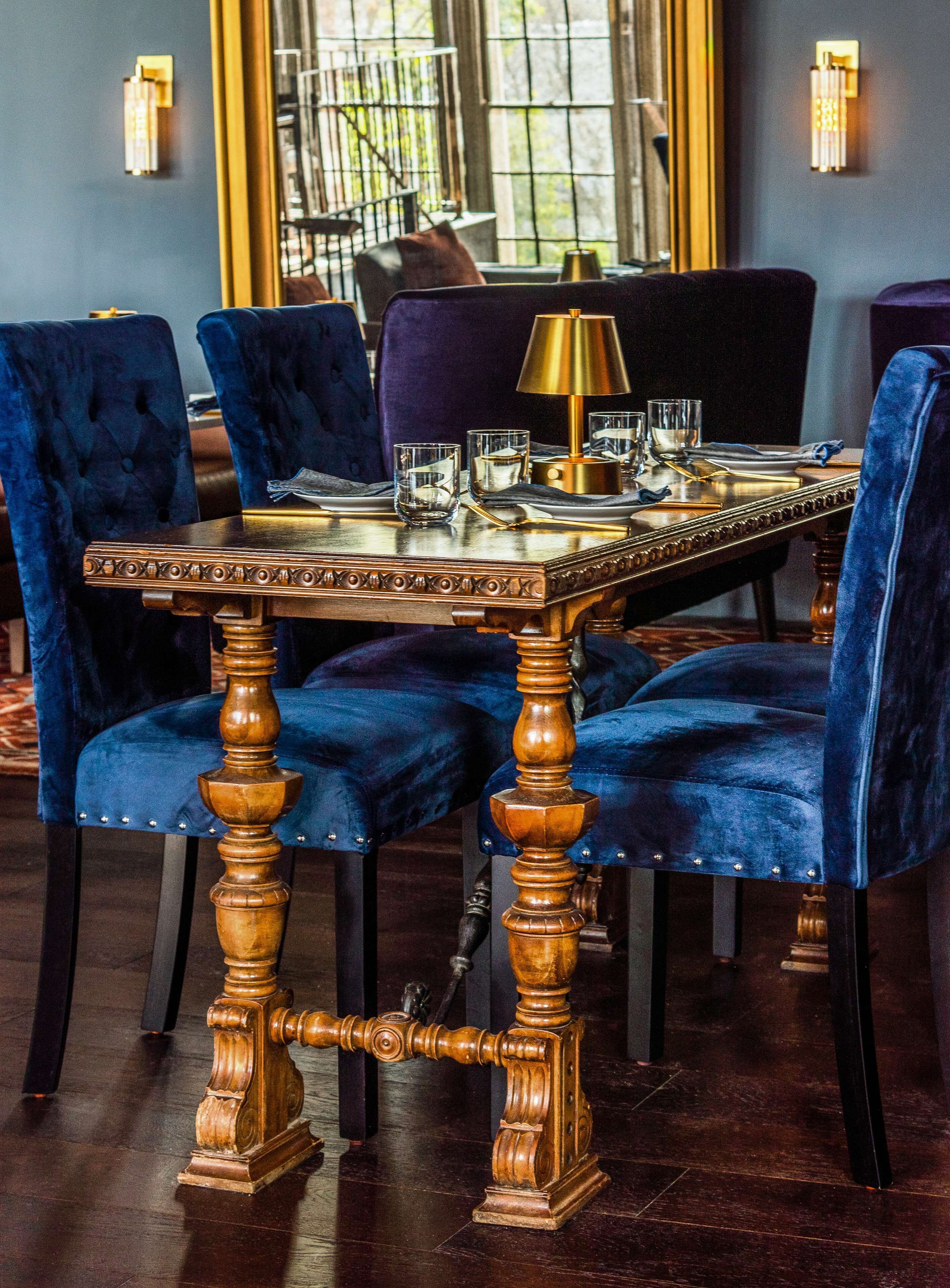 A dining table with ornate wooden legs, surrounded by velvet chairs.