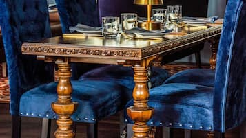 A dining table with ornate wooden legs, surrounded by velvet chairs.