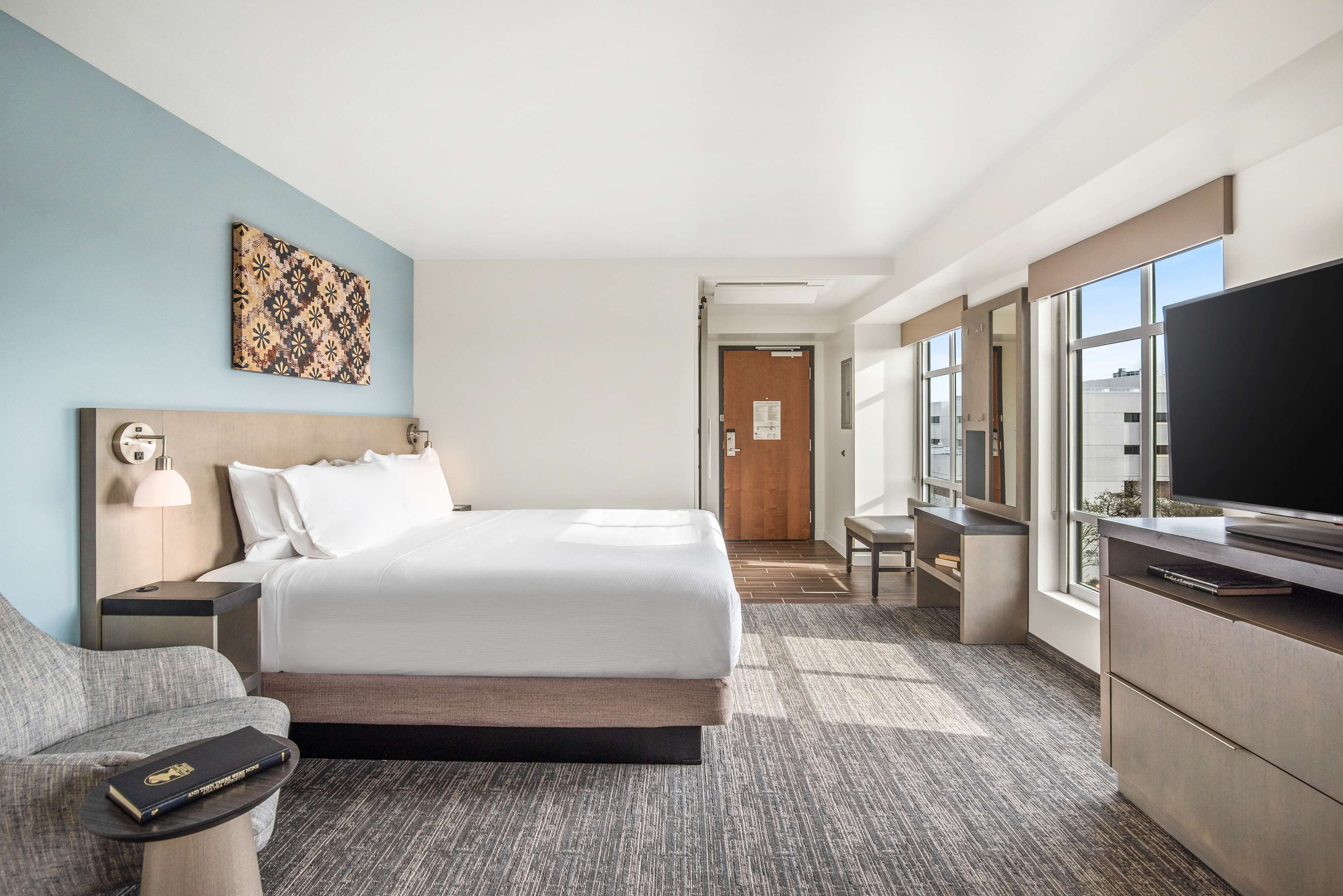 A hotel room with a bed, a desk, a television, a chair, and a small table.