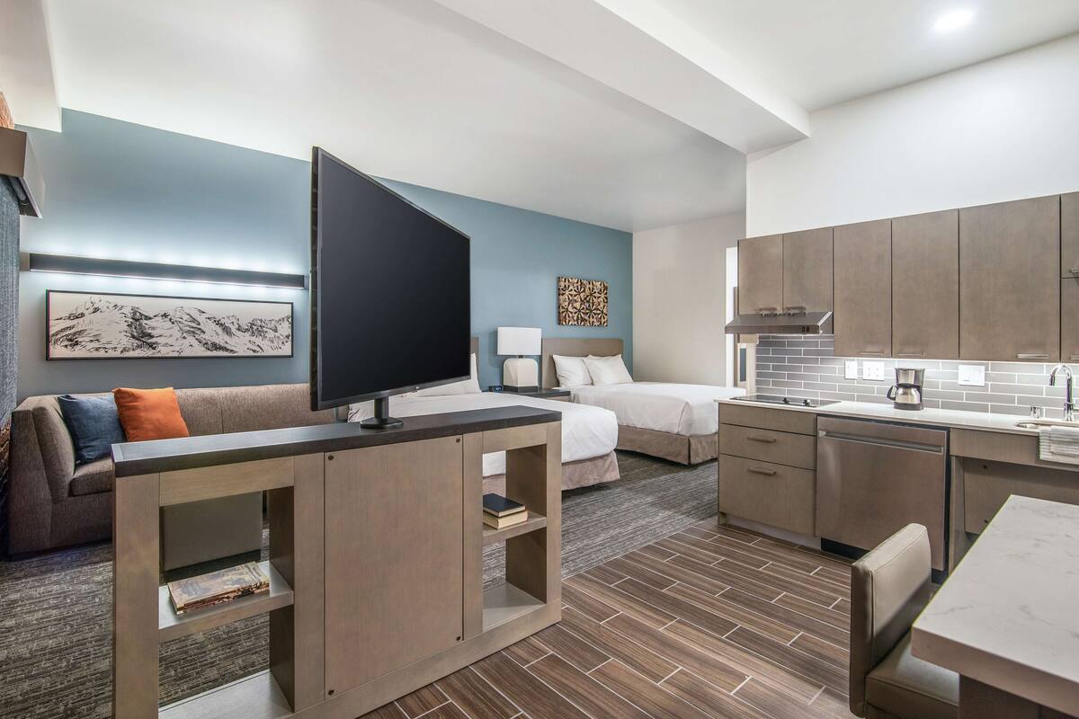 Een moderne hotelkamer met televisie, bank, bed en kitchenette.