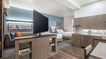 A modern hotel room with a TV, sofa, bed, and kitchenette.
