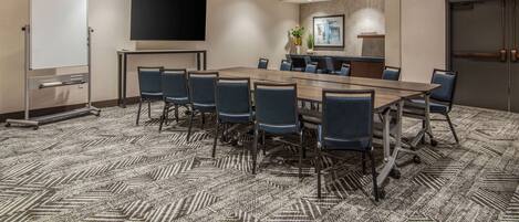 A conference room with a long table, chairs, a whiteboard, a flat-screen TV, and a carpeted floor.