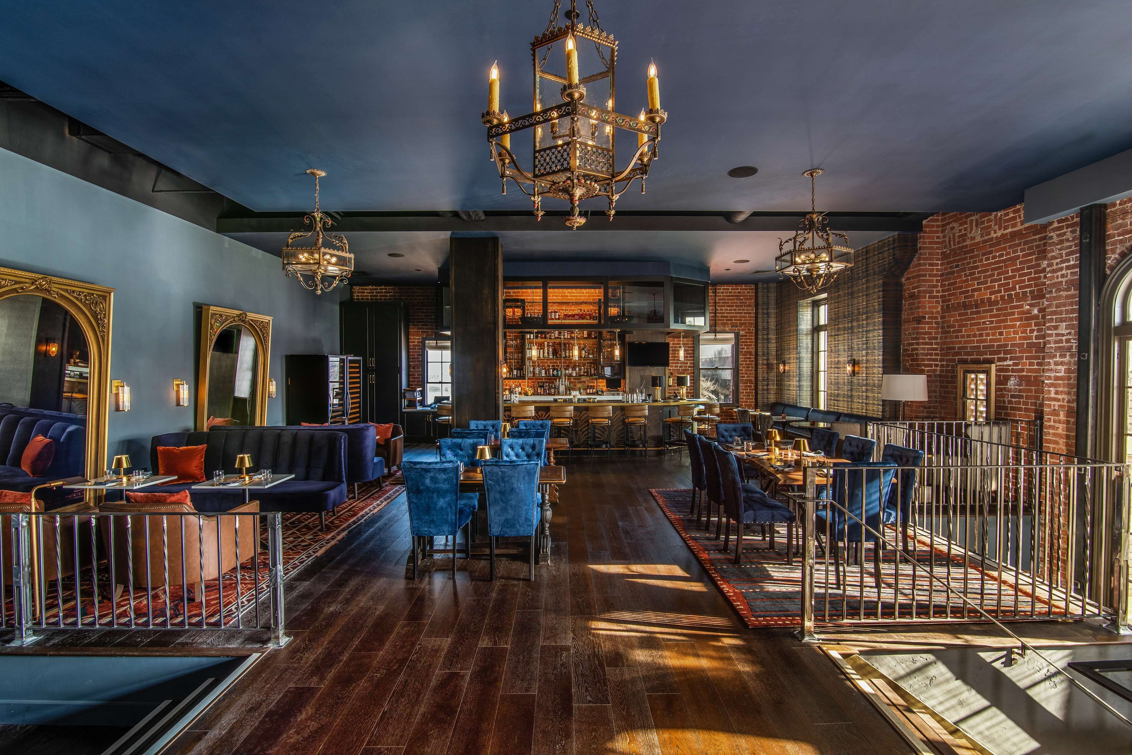 A spacious bar area with high ceilings and exposed brick walls, featuring a central bar counter and seating arrangements.