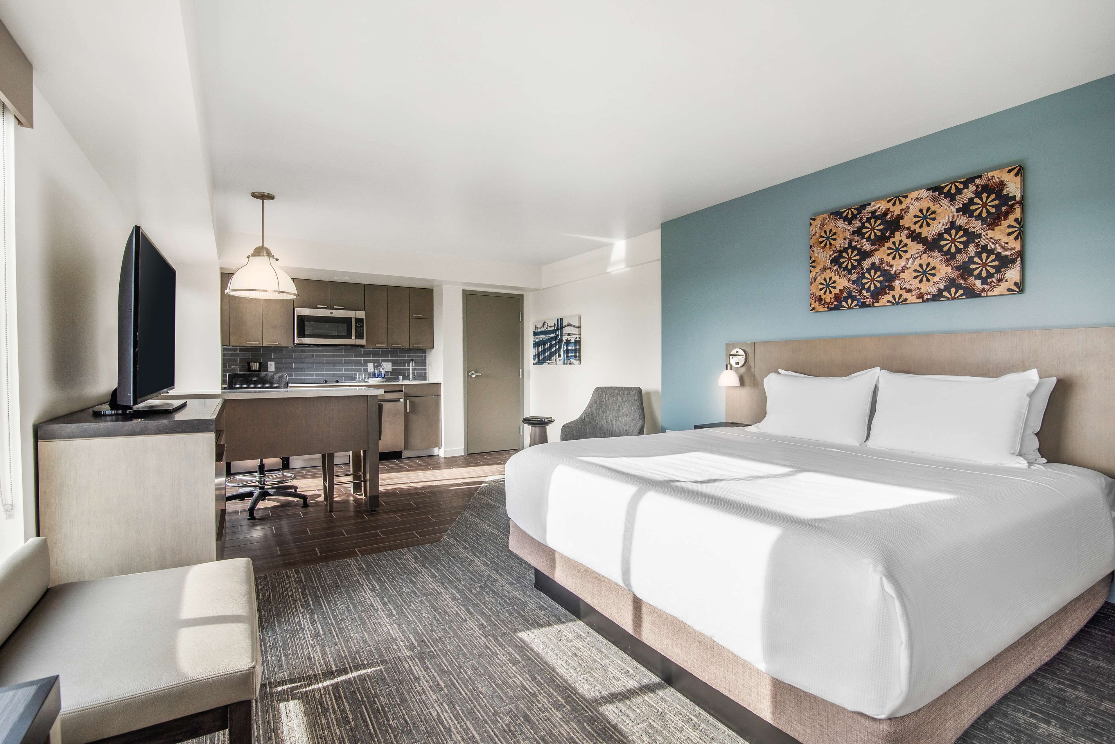 A hotel room with a bed, a desk, a chair, a television, a microwave, and a kitchen area.