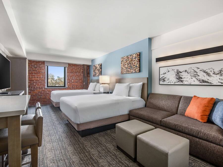 A hotel room with two beds, a sofa, a desk, and a TV.